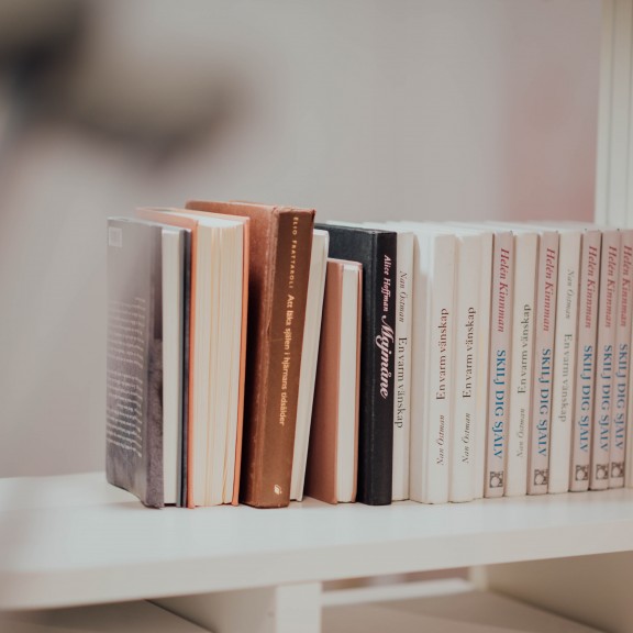 A photo of books stacked upright on top of a white shelf